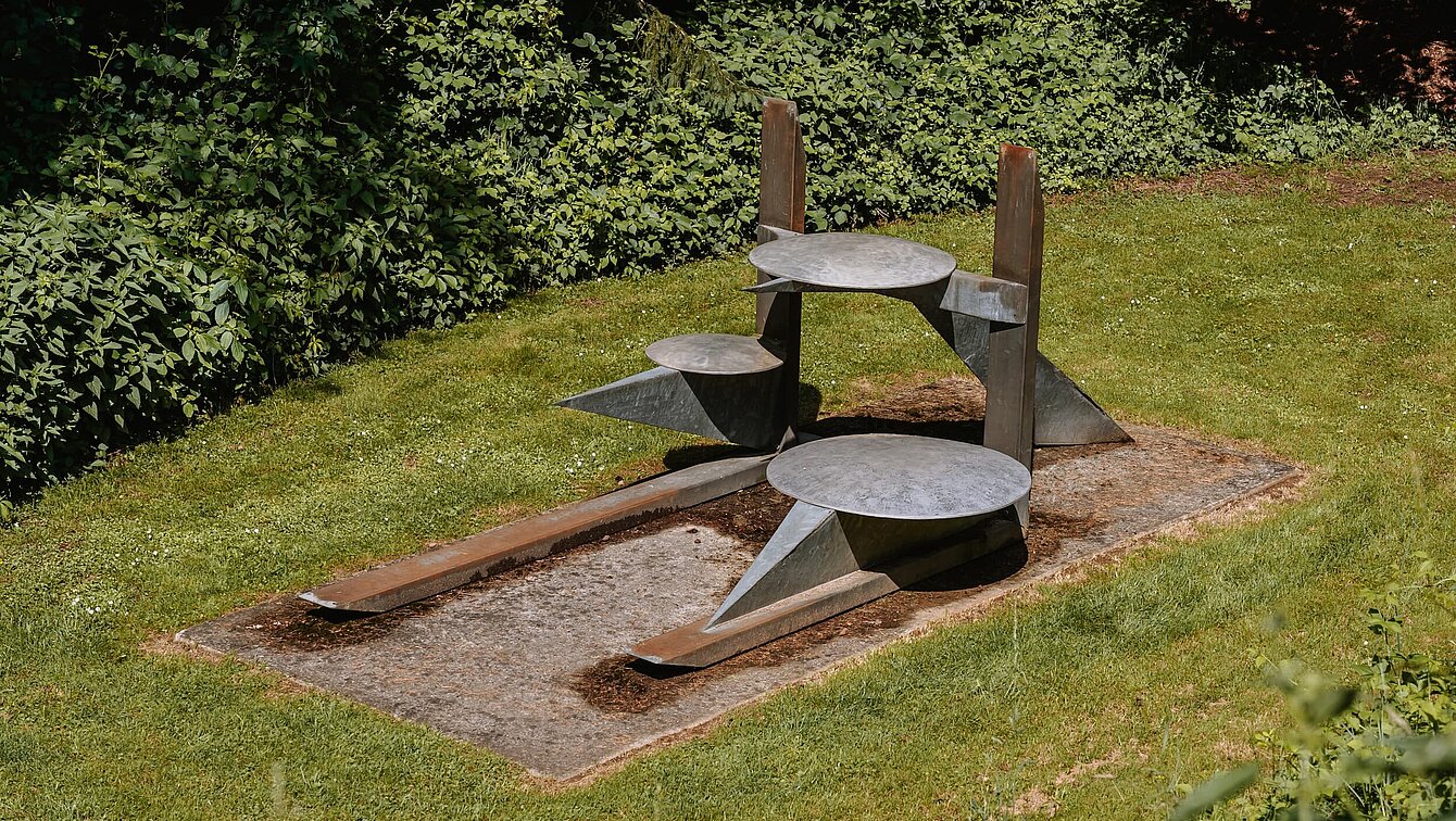 Das Zentrum der Skulptur bilden die beiden vertikalen und horizontalen Träger, auf die sich die Konstruktion stützt. Die Formen scheinen sich in einem fein ausbalancierten Gleichgewicht zu befinden und strahlen trotz der Schwere des Materials eine gewisse Leichtigkeit aus. Ihre konkrete Bedeutung gewinnt die Arbeit aus Vergleichen der einzelnen Bestandteile der Skulptur mit allgemein bekannten Objekten.