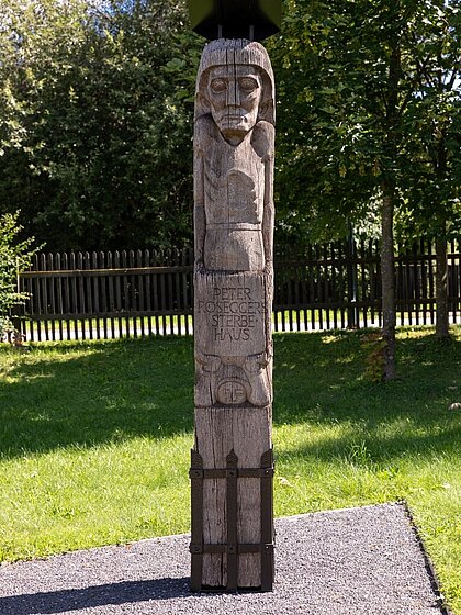 Holzsäule mit geschnitzten Elementen in metallener Halterung.