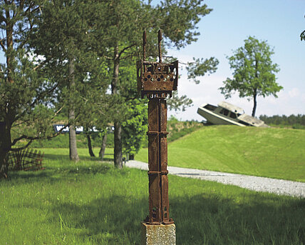 Gerhard Moswitzers Metallskulptur steht auf einem Rasenstück des Berggartens. Im Hintergrund sieht man verschwommen weitere Skulpturen. 