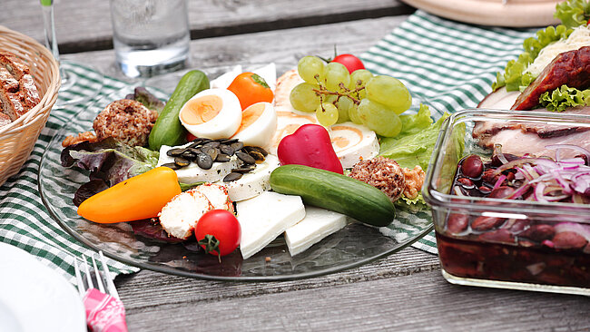 Ein Teller mit Kathreiner Bio-Ziegenkäsevariation und eine Schüssel mit steirischem Käferbohnensalat auf einem Holztisch platziert
