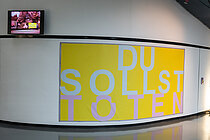 Blick auf das gelbe Banner der Installation "Du sollst töten"