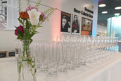 Glasses as well as a vase with flowers stand on a bar in the foyer in the Joanneumsquarter.