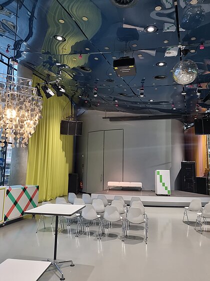 In Space04 at Kunsthaus Graz, there is a 40-seater movie theater in front of the stage. Behind it are high tables. At the podium is a lectern and sofas with a coffee table. 