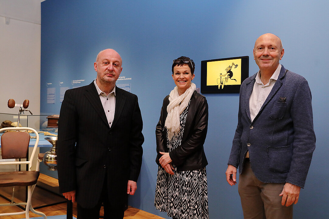 Two men and a woman standing in front of a blue wall.