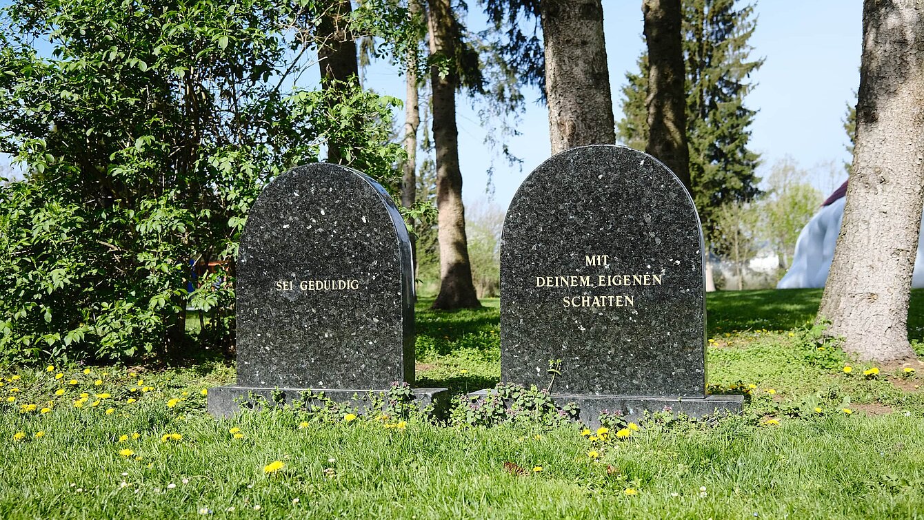 Two gravestones made of smooth stone. The inscription on the first: "Be patient". The inscription on the second: "With your own shadow" [inscriptions are translated from German].