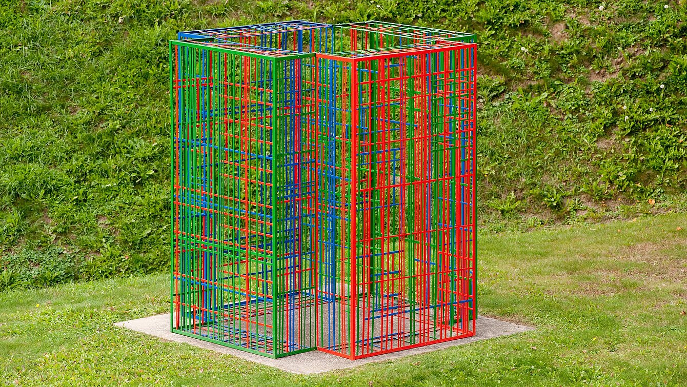 The sculpture consists of colored metal struts and stands on a plinth. Four colored metal modules overlap and network differently depending on the viewing angle.