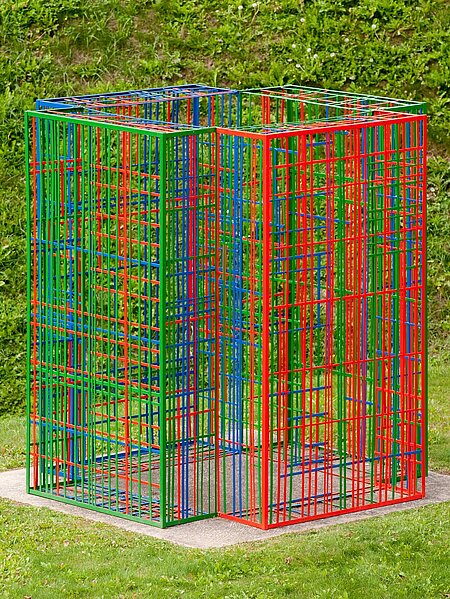 The sculpture consists of colored metal struts and stands on a plinth. Four colored metal modules overlap and network differently depending on the viewing angle.