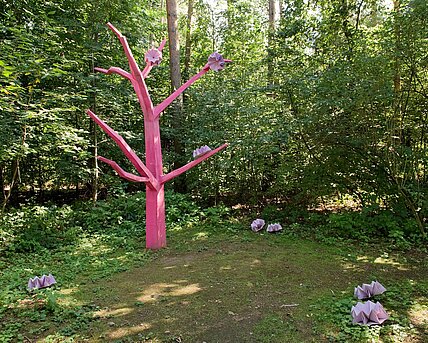 The sculpture "Antisocial daughter" stands as an abstract and reduced tree form between mixed forest trees and within the undergrowth and bushes of a clearing.