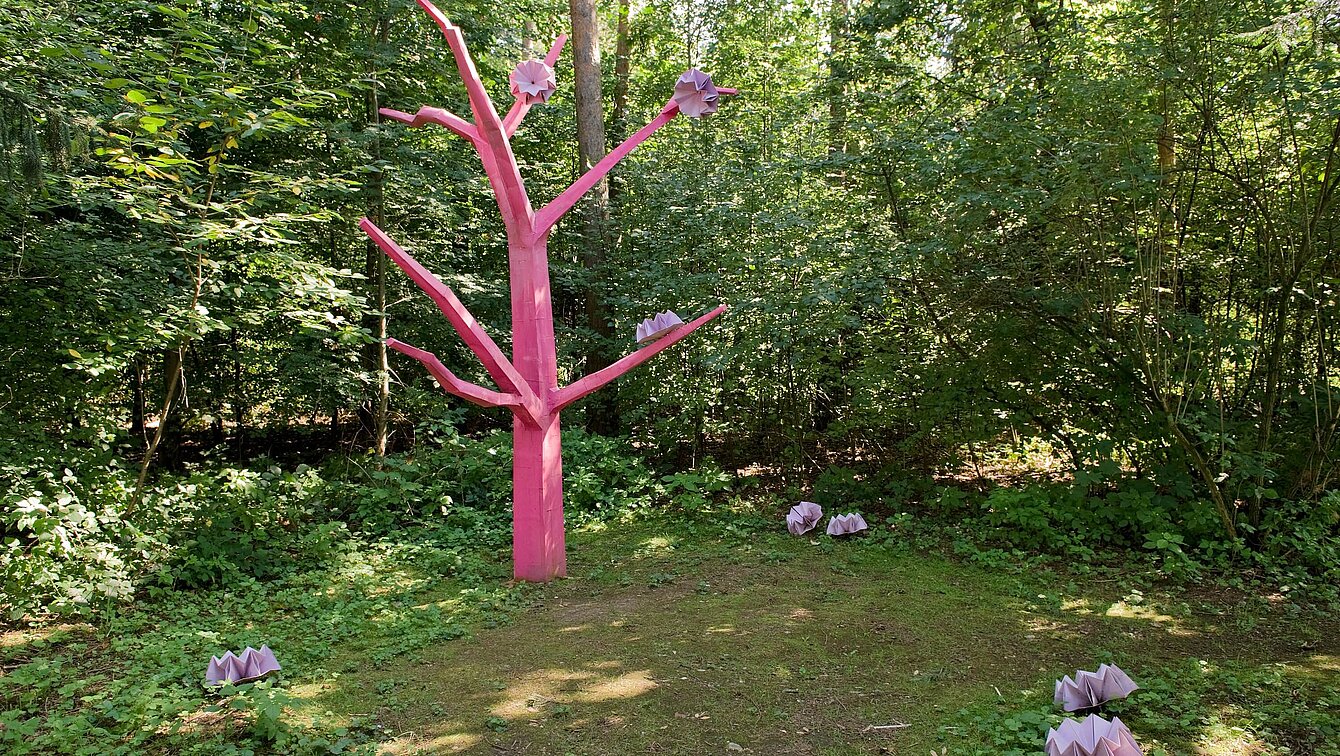 Die Skulptur Asoziale Tochter steht als abstrahierte und reduzierte Baumform zwischen Mischwaldbäumen und innerhalb des Unterholzes und Gebüsches einer Lichtung.