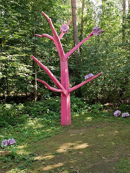 Die Skulptur Asoziale Tochter steht als abstrahierte und reduzierte Baumform zwischen Mischwaldbäumen und innerhalb des Unterholzes und Gebüsches einer Lichtung.