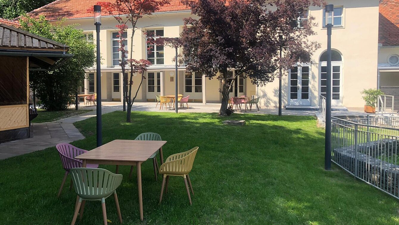 Blick Richtung Heimatsaal im Duftgarten. Im Vordergrund ist ein Tisch mit Sesseln, seitlich sieht man den Pavillon.