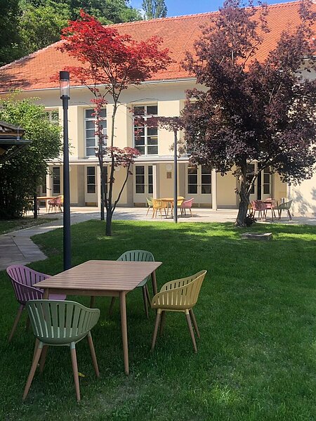 Blick Richtung Heimatsaal im Duftgarten. Im Vordergrund ist ein Tisch mit Sesseln, seitlich sieht man den Pavillon.