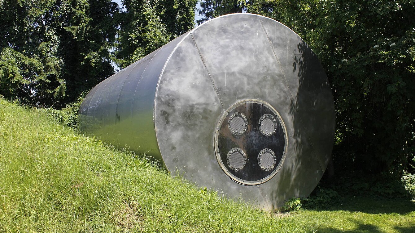 A former steel water silo (11 m long, 4 m in diameter) was reinterpreted by media artist and musician Pinter. It forms the basic structure of this sculpture. Eight integrated bass loudspeakers transform the silo into a musical instrument. The low frequency ranges generate pressure waves that make the sound not only audible but also physically tangible.