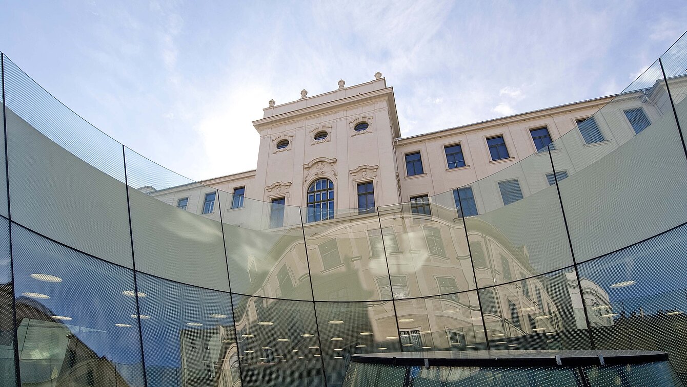 Im Vordergrund ist ein gläserner Trichter des Joanneumsviertels, im Hintergrund die Fassade der Neuen Galerie zu sehen.