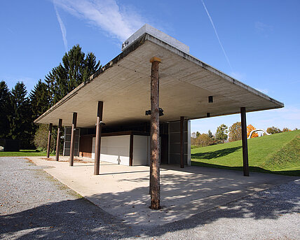 A white Carrara marble block lies on the edge of the roof of the Berggarten café. It is supported by a tree trunk that at first glance seems out of place. 