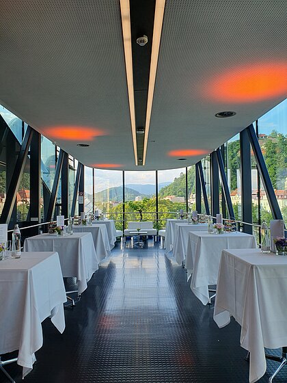 In the Needle there are bar tables with white tablecloths for a reception. On the tables are set flowers, drinks and etagères with appetizers.