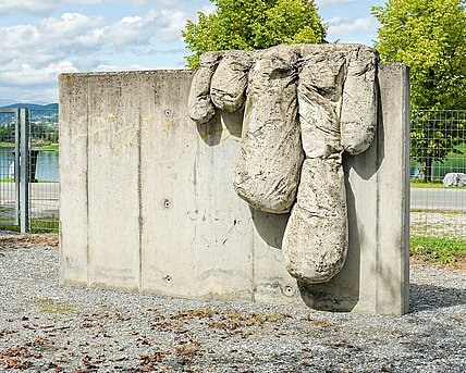 Die Skulptur des Malers Bohatsch ist eine senkrechte, glatte Betonplatte mit herabhängenden "Tropfen" aus Beton. Diese ähneln Fingern und sollen das langsam über die Leinwand kriechende Rinnen der Farbe simulieren.