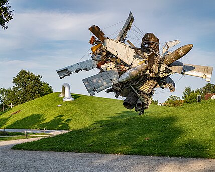 Blick vom Wegesrand auf die Skulptur "Airplane Parts & Hills" von Nancy Rubins und "Die Erdkugel als Koffer" von Peter Weibel in der Ferne