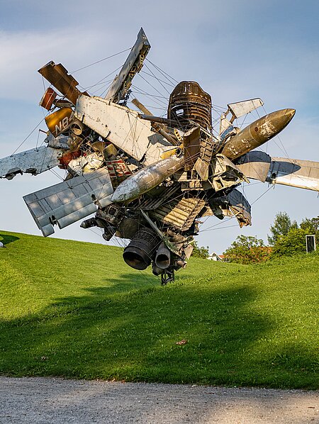 Blick vom Wegesrand auf die Skulptur "Airplane Parts & Hills" von Nancy Rubins und "Die Erdkugel als Koffer" von Peter Weibel in der Ferne