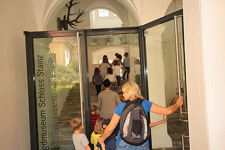 Erwachsene und Kinder betreten das Museum durch die Glaseingangstüre
