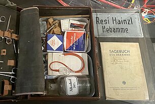 Zu sehen ist der Hebammenkoffer von Frau Resi Hainzl sowie ein Tagebuch.
