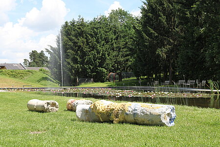 Mehrere säulenartige Teile aus Beton und PU-Schaum liegen im Gras.