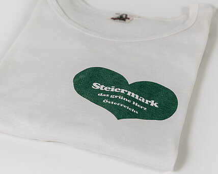 Zu sehen ist ein weißes T-Shirt, bedruckt mit dem grünen Herz der Steiermark .