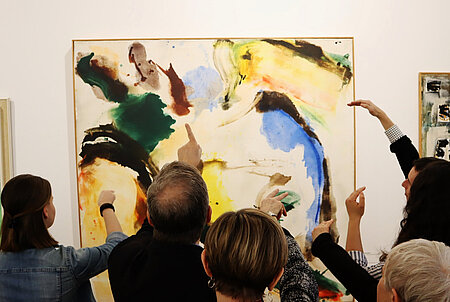 Menschen stehen vor einem Gemälde zusammen, richten den Blick darauf und zeigen in verschiedene Richtungen.