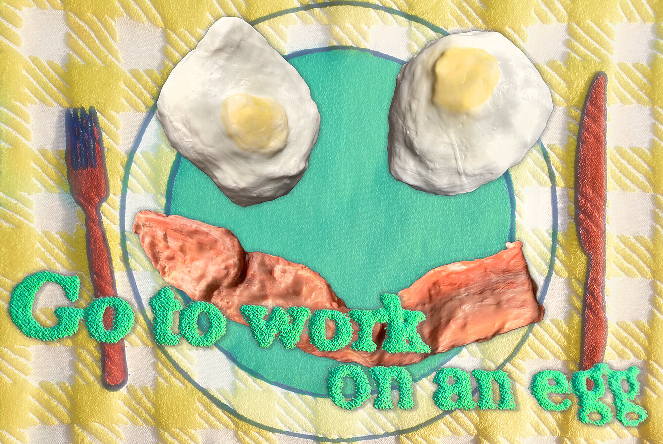 Ein grüner Schriftzug "go to work on an egg" vor zwei Spiegeleier- und Speckskulpturen, die auf einem Teller aus Stoff liegen. Daneben eine Gabel und ein Messer aus Stoff.