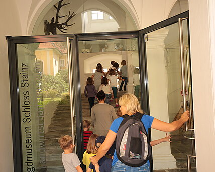 Erwachsene und Kinder betreten das Museum durch die Glaseingangstüre