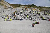 Erlebnis Erdgeschichte Personen unterschiedlichen Alters in gelben Warnwesten auf einem Geröllfeld des Steinbruchs, bei der Suche nach Fossilien.