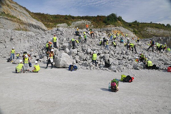 Erlebnis Erdgeschichte Personen unterschiedlichen Alters in gelben Warnwesten auf einem Geröllfeld des Steinbruchs, bei der Suche nach Fossilien.
